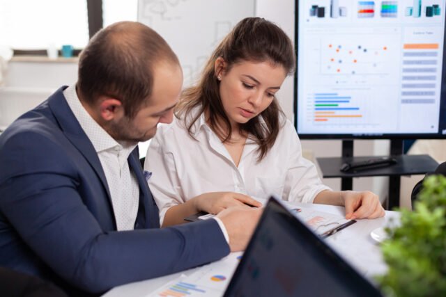 Colleagues of startup business discussing looking at documents Project Management Assignment Help
